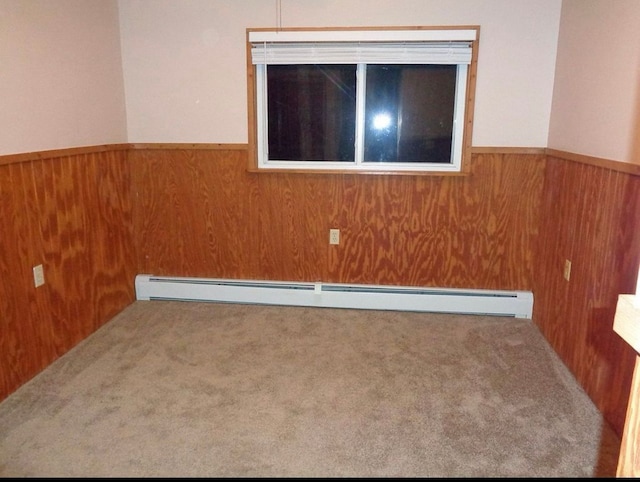 spare room with carpet flooring, baseboard heating, wood walls, and wainscoting