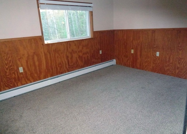 carpeted spare room featuring a wainscoted wall, baseboard heating, and wooden walls