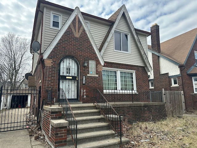 tudor-style house with a gate, fence, and brick siding