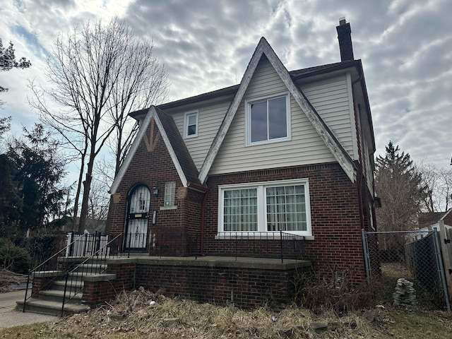 tudor house featuring brick siding, a chimney, and fence