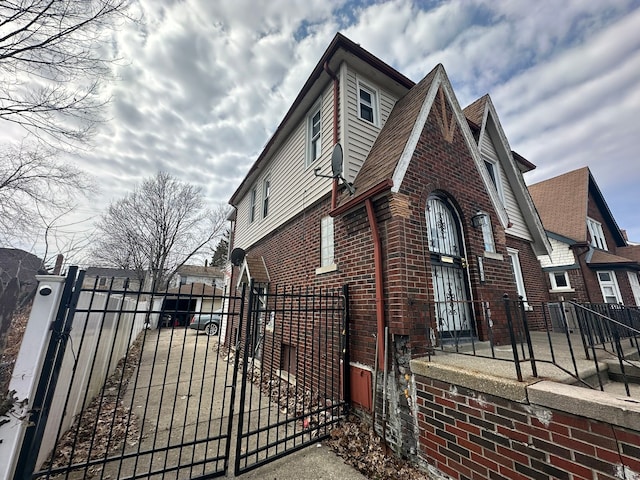 view of side of home with a gate, fence, and brick siding