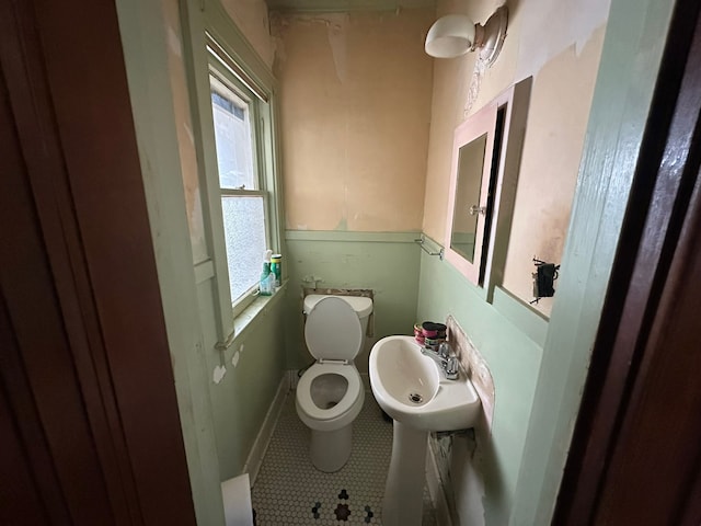 half bathroom featuring tile patterned flooring, toilet, baseboards, and a sink