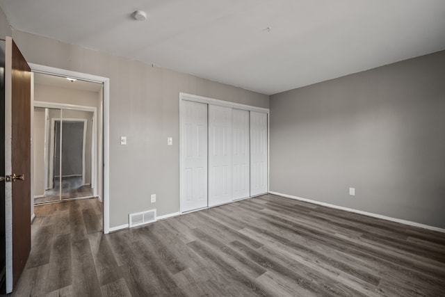 unfurnished bedroom featuring visible vents, baseboards, a closet, and dark wood finished floors