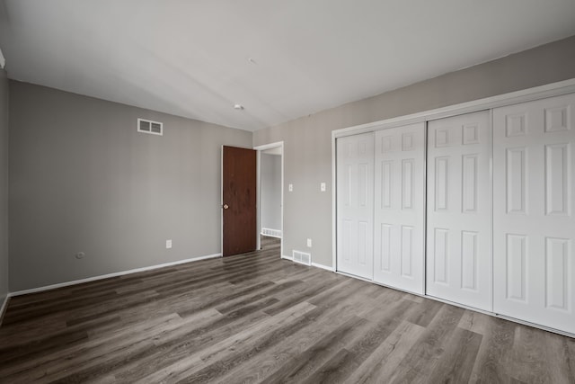 unfurnished bedroom with dark wood-style floors, visible vents, a closet, and baseboards