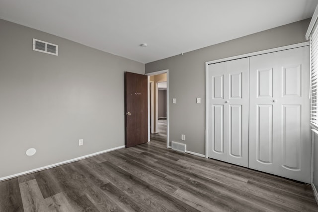 unfurnished bedroom featuring dark wood-type flooring, baseboards, visible vents, and a closet