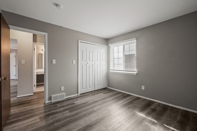 unfurnished bedroom with visible vents, baseboards, dark wood-type flooring, and a closet