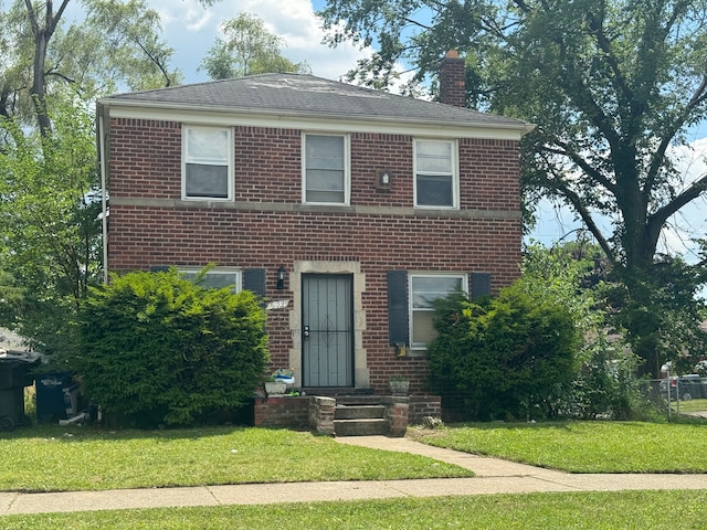 view of front of home with brick siding, a chimney, and a front yard