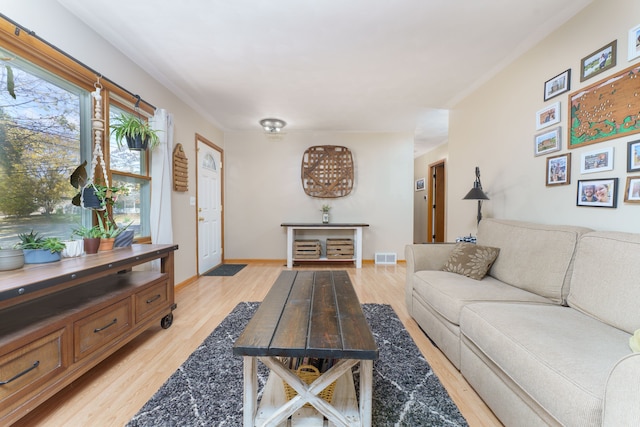 living room with light wood-style flooring, visible vents, and baseboards