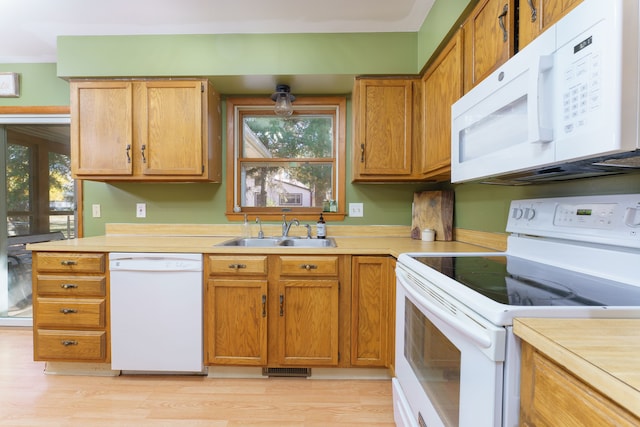 kitchen with a sink, white appliances, light wood-style flooring, and light countertops