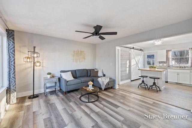 living room featuring a barn door, a ceiling fan, baseboards, and light wood finished floors