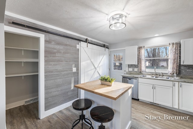 kitchen with a breakfast bar area, butcher block countertops, a sink, stainless steel dishwasher, and a barn door