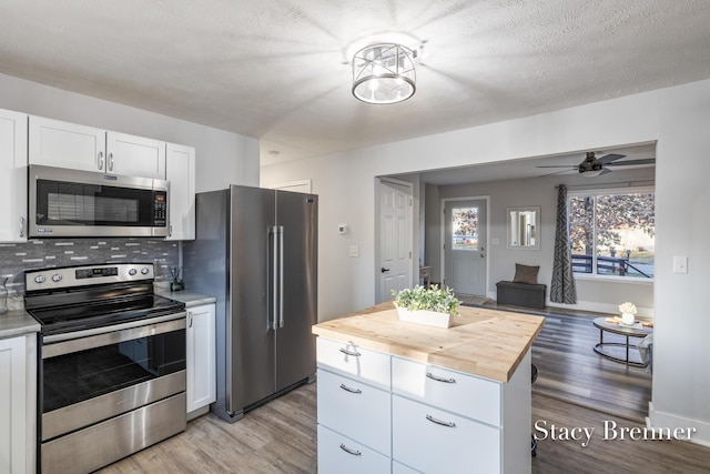 kitchen with stainless steel appliances, white cabinets, light wood-style floors, tasteful backsplash, and butcher block counters