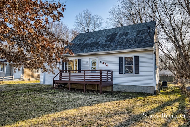 view of front of home with a wooden deck, an attached garage, a shingled roof, and a front yard