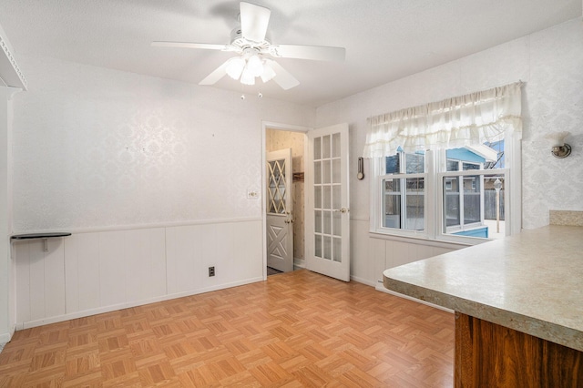 unfurnished dining area featuring a ceiling fan, wainscoting, and a textured ceiling