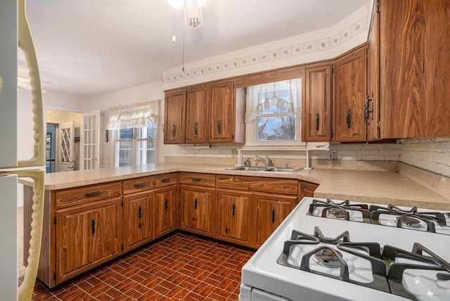 kitchen with light countertops, a peninsula, white gas range, and a sink