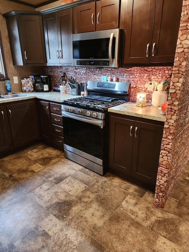 kitchen with a sink, decorative backsplash, dark brown cabinetry, stone finish floor, and appliances with stainless steel finishes