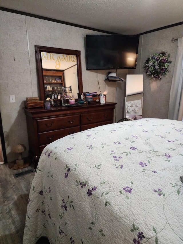 bedroom with crown molding, wood finished floors, visible vents, and a textured ceiling