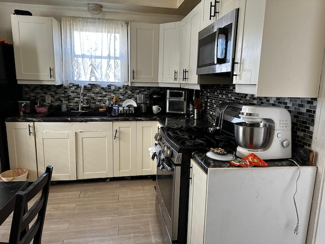 kitchen featuring light wood-type flooring, a sink, backsplash, white cabinetry, and appliances with stainless steel finishes