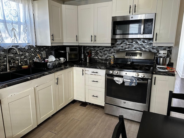 kitchen with a sink, backsplash, wood finished floors, appliances with stainless steel finishes, and white cabinets