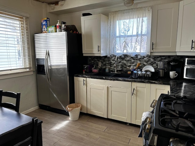 kitchen featuring a sink, black gas range, decorative backsplash, and stainless steel fridge with ice dispenser