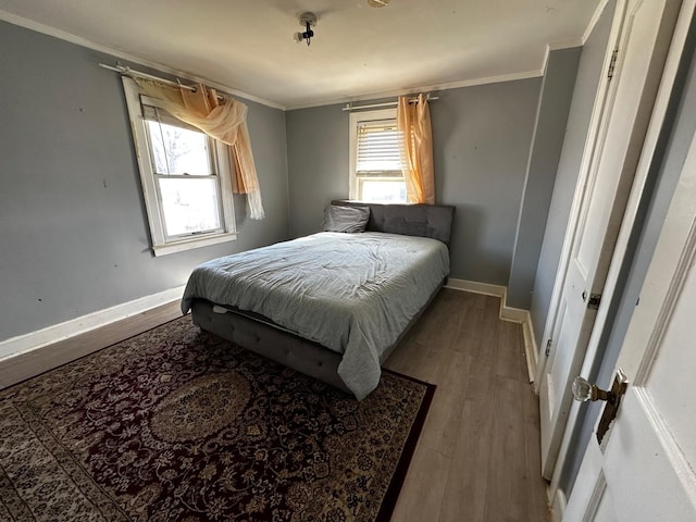 bedroom featuring multiple windows, wood finished floors, baseboards, and ornamental molding