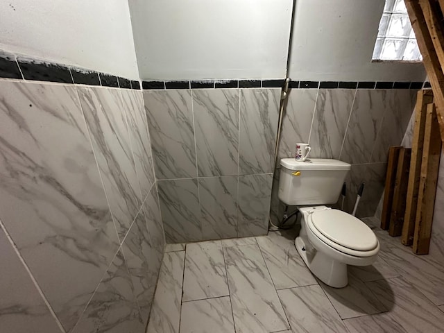 half bath with marble finish floor, toilet, and tile walls