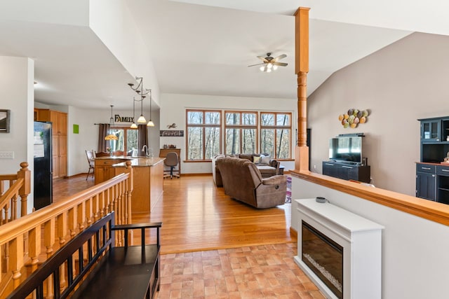 living area featuring baseboards, ceiling fan, vaulted ceiling, light wood-style floors, and a glass covered fireplace