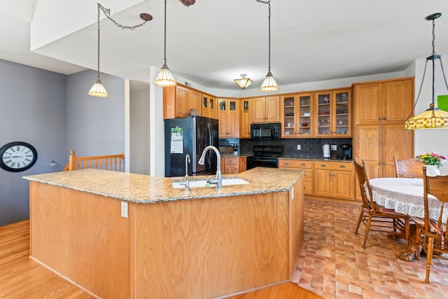 kitchen with tasteful backsplash, light stone countertops, decorative light fixtures, black appliances, and a sink