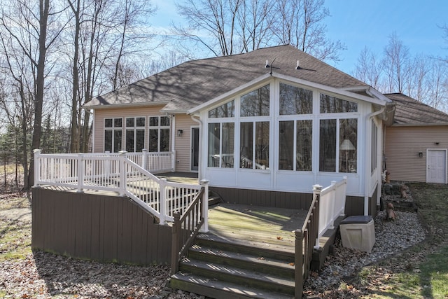 rear view of property featuring a wooden deck, a shingled roof, and a sunroom