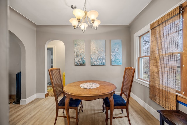 dining room featuring an inviting chandelier, light wood-style floors, arched walkways, and baseboards