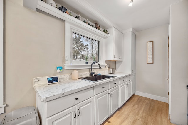 kitchen featuring white cabinets, light wood-style floors, baseboards, and a sink