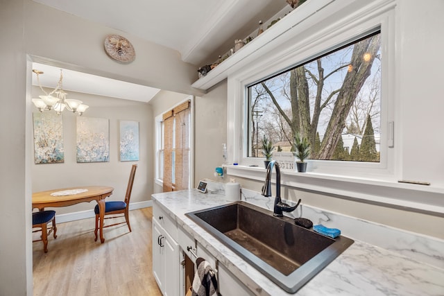 kitchen with baseboards, a sink, light wood-style floors, white cabinetry, and a notable chandelier