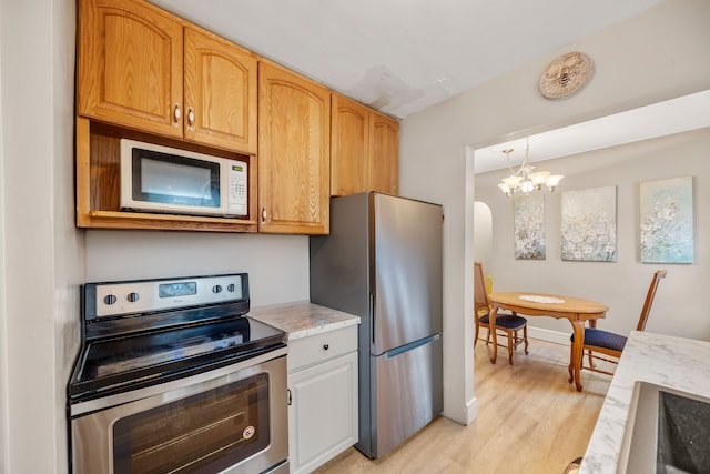 kitchen featuring light wood finished floors, hanging light fixtures, arched walkways, a notable chandelier, and stainless steel appliances