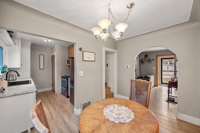 dining area with light wood finished floors, visible vents, stairs, arched walkways, and a notable chandelier