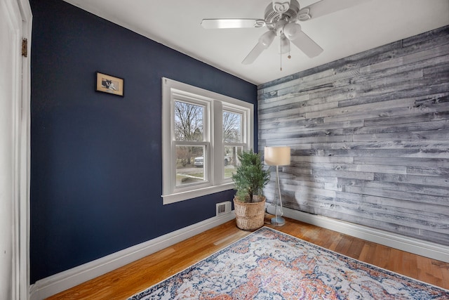 sitting room with visible vents, an accent wall, baseboards, wood finished floors, and a ceiling fan