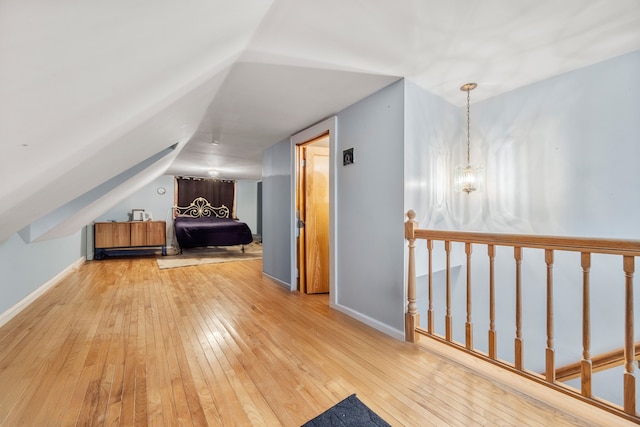 additional living space with baseboards, wood-type flooring, a notable chandelier, and vaulted ceiling