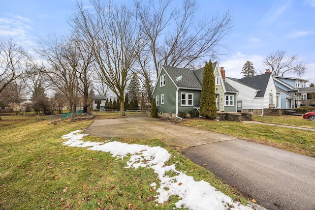 view of side of home featuring a lawn, a chimney, driveway, and fence