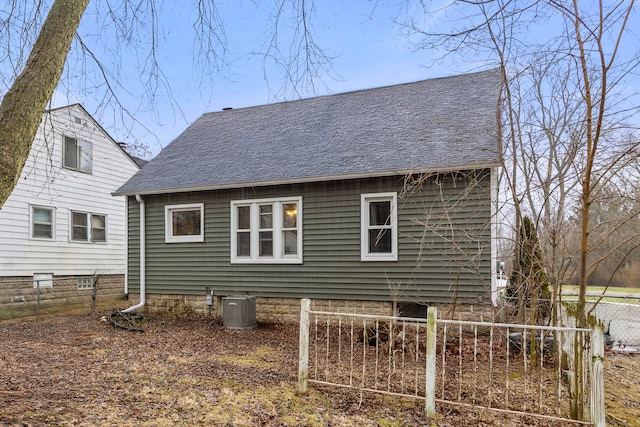 back of house with central air condition unit, fence, and roof with shingles