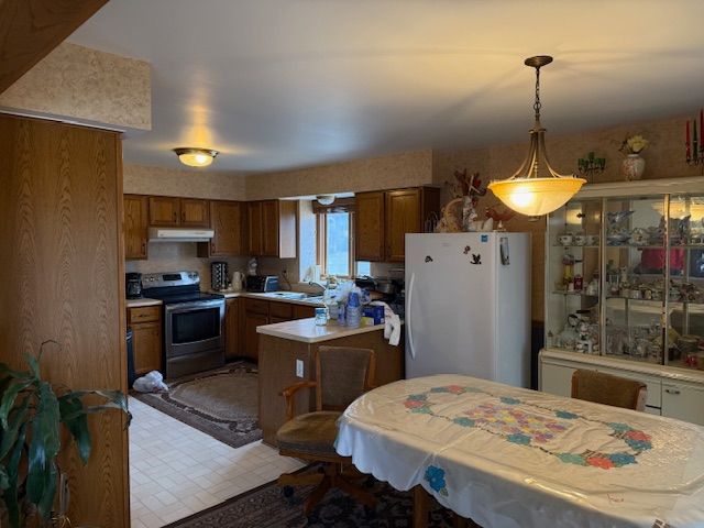 kitchen with brown cabinets, under cabinet range hood, freestanding refrigerator, light countertops, and stainless steel electric range oven