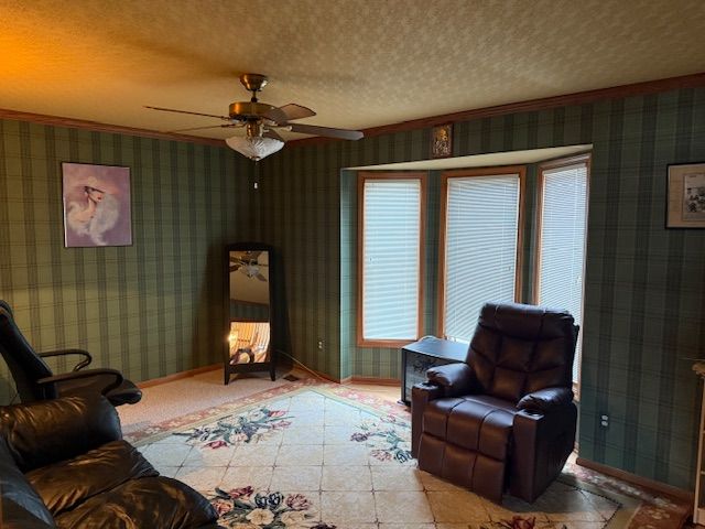 living area featuring a textured ceiling, wallpapered walls, baseboards, and a ceiling fan