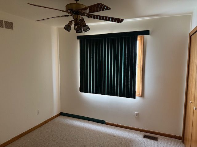 unfurnished room featuring visible vents, baseboards, light colored carpet, and a ceiling fan