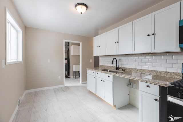 kitchen featuring baseboards, light stone counters, decorative backsplash, white cabinetry, and a sink