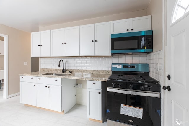 kitchen with stainless steel gas range oven, backsplash, light stone countertops, white cabinets, and a sink