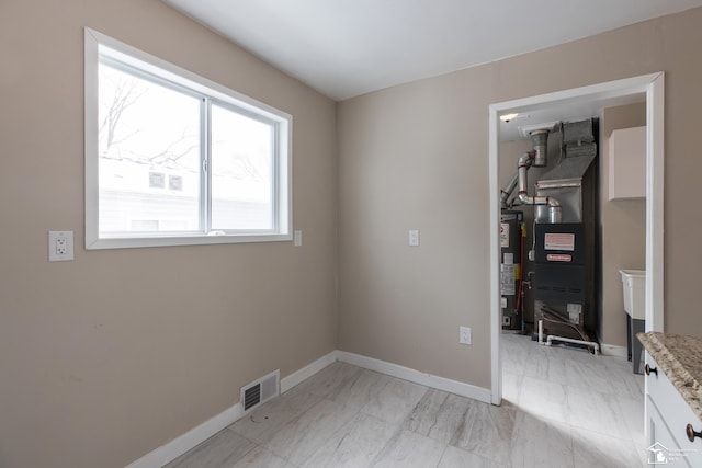 empty room featuring gas water heater, visible vents, baseboards, and marble finish floor