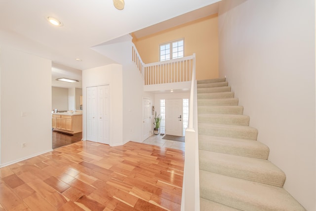 foyer entrance featuring stairway, light wood-style floors, baseboards, and a towering ceiling