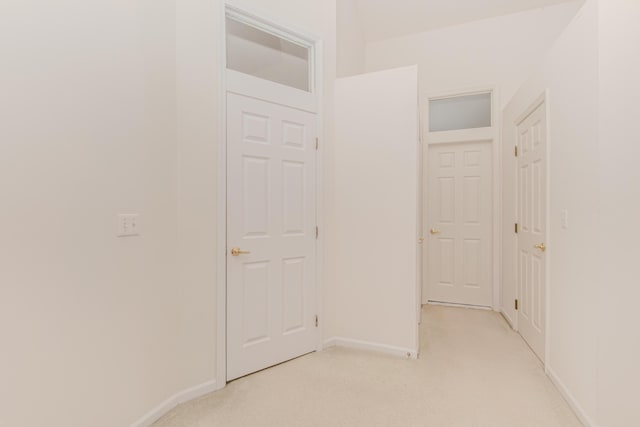 hallway with baseboards and light colored carpet