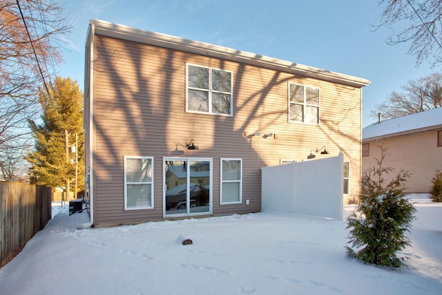 snow covered rear of property featuring central AC unit and fence