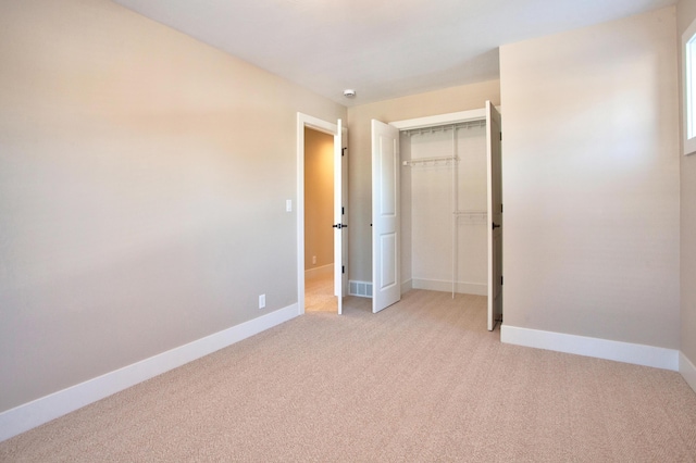 unfurnished bedroom featuring visible vents, baseboards, a closet, and light carpet