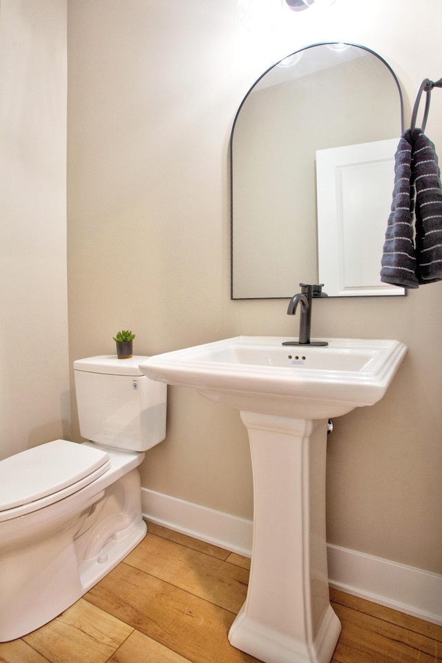 bathroom with toilet, wood finished floors, baseboards, and a sink