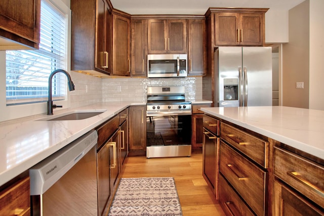 kitchen with a sink, stainless steel appliances, light wood-style flooring, and decorative backsplash